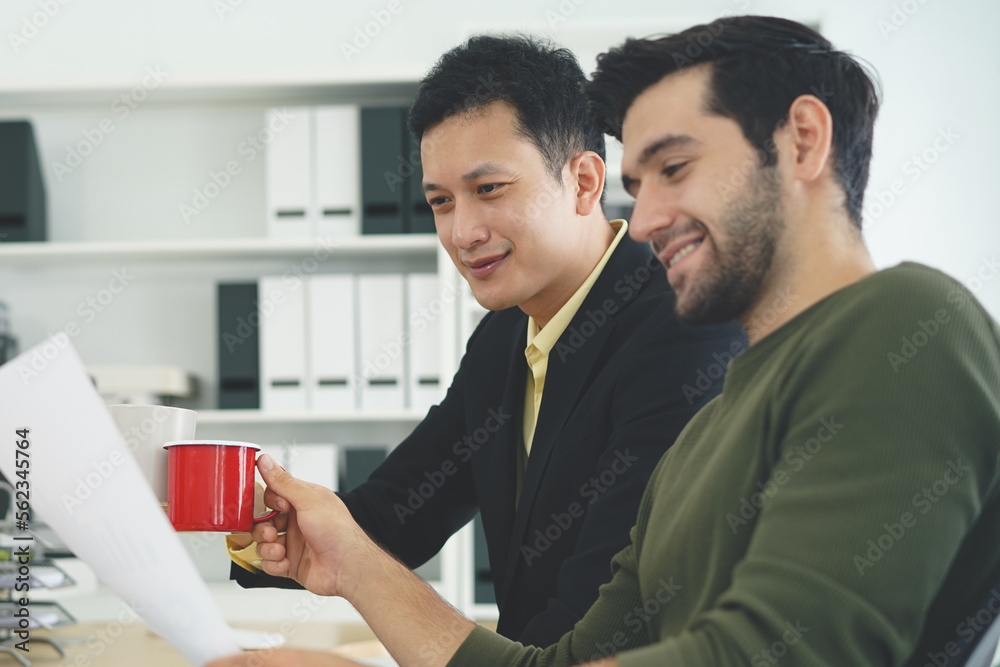 Two men in the office were happy while they were looking at the reports on the papers. And collided coffee mugs to show pride in the good response Two men in the office were happy while they were looking at the reports on the papers. And collided coffee mugs to show pride in the good response