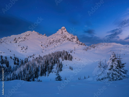 Beautiful night winter landscape in the mountains. Vibrant night sky with stars and clouds.