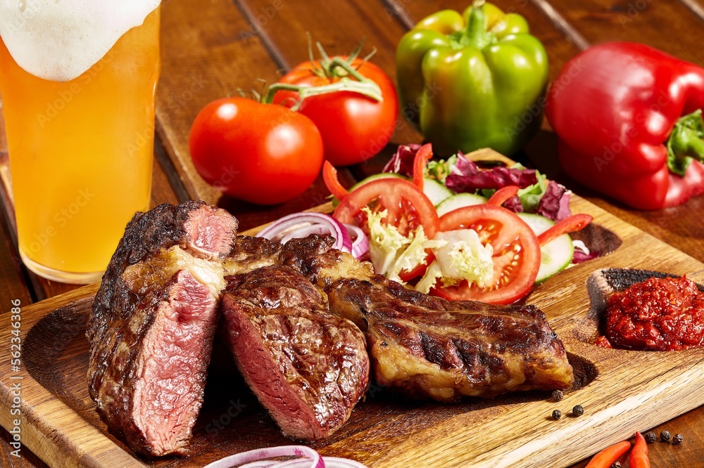 Cote de bœuf avec ses légumes en sur plancha et verre de bière sur un fond de