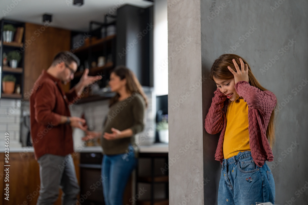 Broken-hearted child covering her ears due to the family fight. Pregnant woman in a conflict with her husband, shouting at each other, having a problem in their marriage.