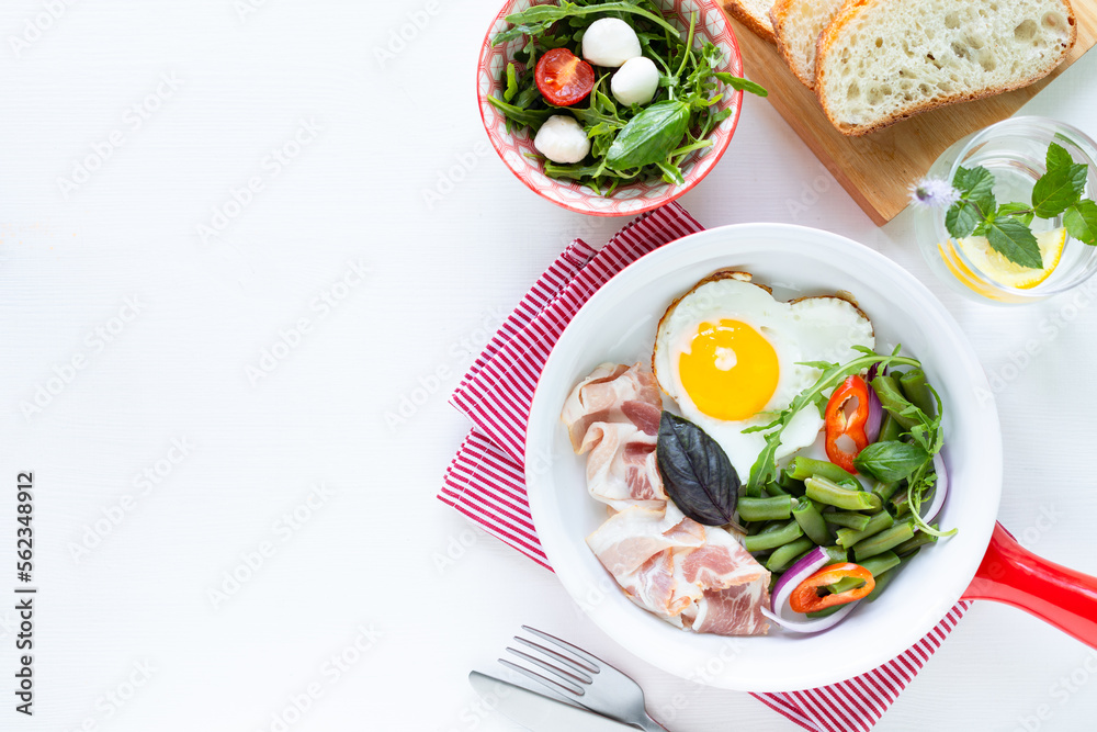 European breakfast: heart shaped egg, bacon, green beans on a white table. Selective focus. View from above. Copy space European breakfast: heart shaped egg, bacon, green beans on a white table. Selective focus. View from above. Copy space