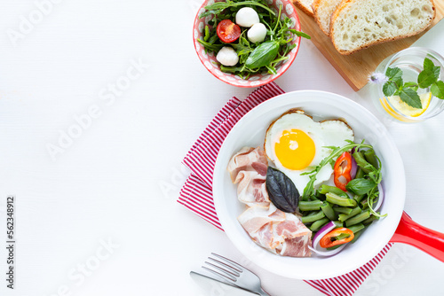 European breakfast: heart shaped egg, bacon, green beans on a white table. Selective focus. View from above. Copy space © Карина Клачук