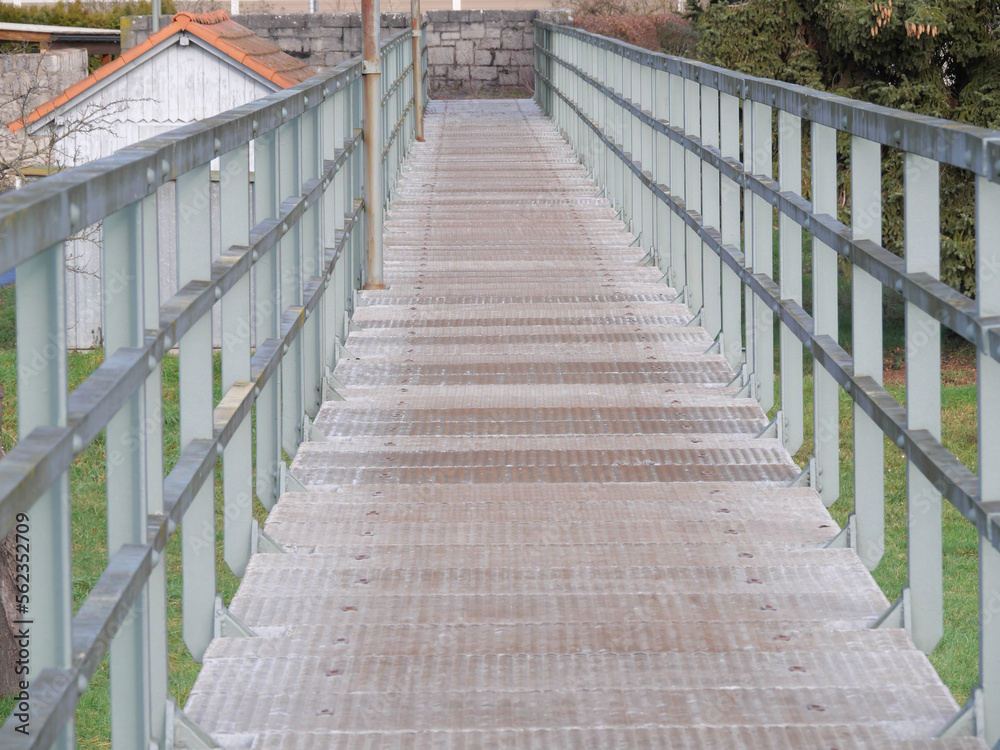 Perspektive Sicht auf eine Fußgängerbrücke mit Stahlgeländer und Gitterrost zur Überquerung einer Überschwämmungsfläche