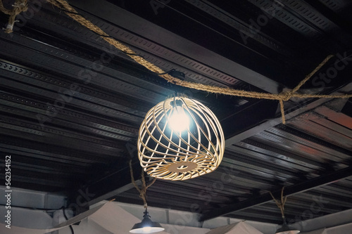 Bottom view of yellow bulb with rattan woven ornament that hanging in the rope. Inspiration for modern lighting and home decoration. Rattan chandelier for vintage and abstract background. Wicker Lamp.