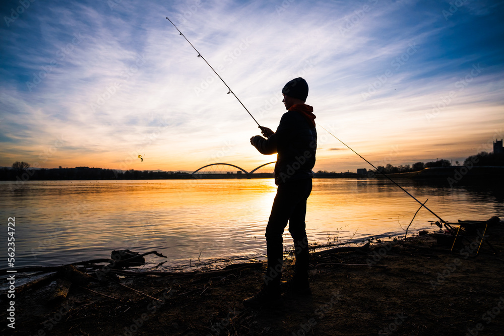 Teenage boy is fishing on river bank. Boy is fishing in sunset.