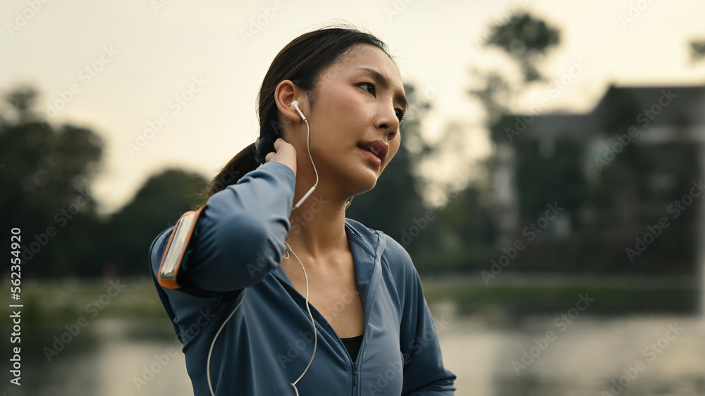 Beautiful athlete woman resting after running outdoor, standing near lake with sunny landscape on background 