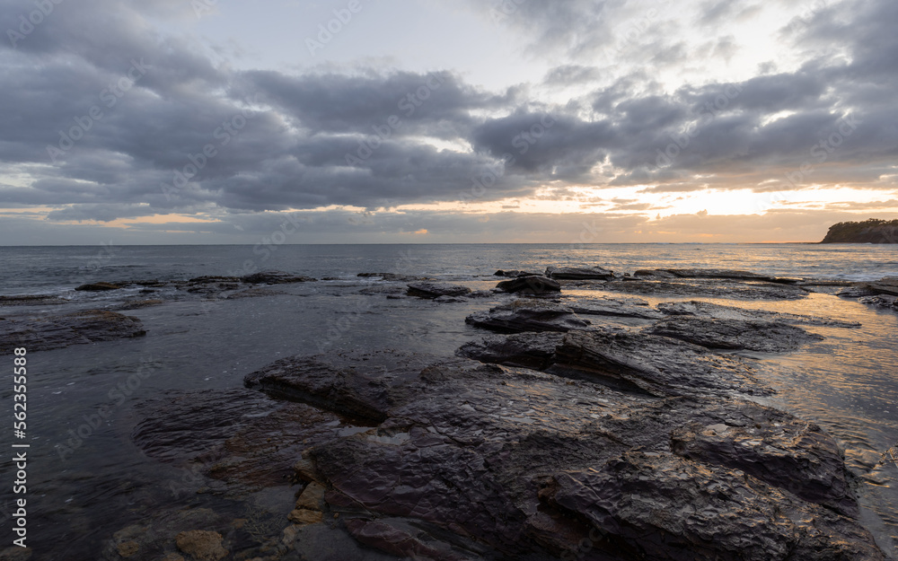 Cloudy sunrise on rocky coastline.