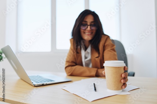 Woman business works in the office at the desk in the office in a beige suit, glasses with a cup of coffee, autumn mood, tiredness coffee break