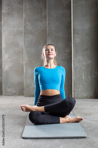 A young woman in sportswear is sitting on a yoga mat with her back and stretching her back muscles. Stretching
