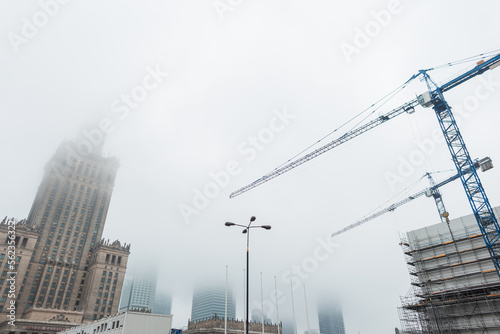 European city Warsaw with the Palace of Culture and construction cranes are building a building in the fog. Real estate, finance and urban background