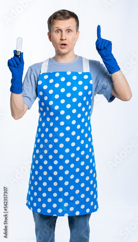 male housewife in blue apron, rubber gloves, blue t-shirt, jeans. the housekeeper is holding a light bulb and thumbs up. idea. White background.