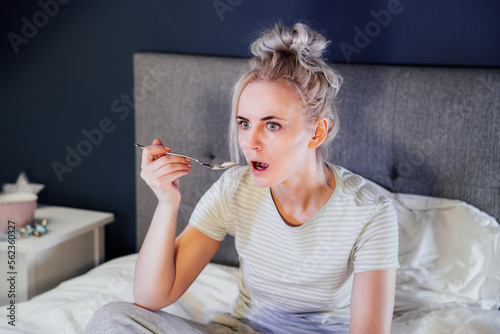 Φωτογραφία Shocked, stressed, surprised woman eating ice cream, holding a remote control while watching TV in bed