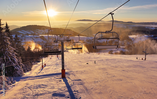 Ski lift empty ropeway on hilghland alpine mountain winter resort on bright sunny evening . Ski chairlift cable way with people enjoy skiing and snowboarding. Sunset sky backlit shining on background photo