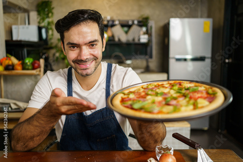 Happy cheerful handsome Italian chef showing a home made baked pizza to camera and smiling.