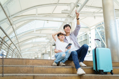 Happy cheerful Asian family traveling in the downtown together concept. Father pointing forefinger to the view and let his son taking a looks.