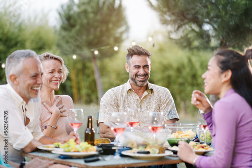 Mature friends having fun together telling jokes and laughing during outdoors dinner in the countryside