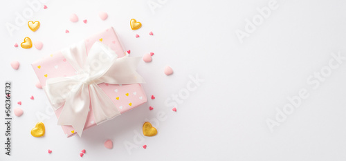 Valentine's Day concept. Top view photo of pastel pink giftbox with silk ribbon bow golden hearts and sprinkles on isolated white background with copyspace