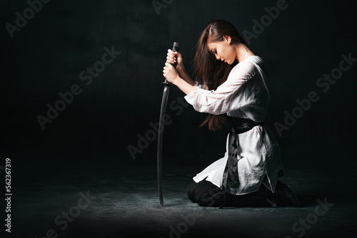 Obraz na płótnie Ninja samurai woman kneeling and sitting on the floor, holding katana sword