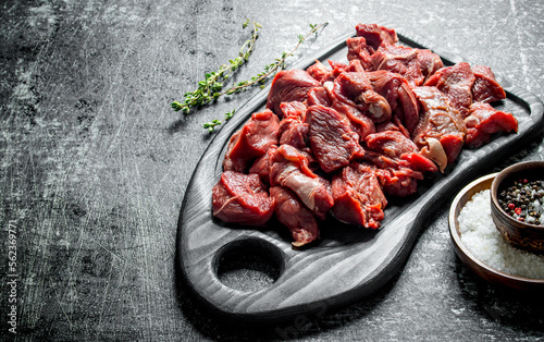 Sliced raw beef on a cutting Board with thyme and seasonings in bowls.