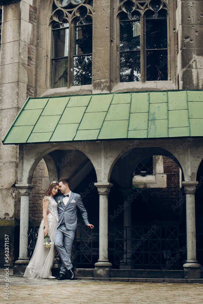 Stylish bride and groom embracing on background of old church. Romantic moment. Provence wedding. Beautiful wedding couple gently hugging in european city.