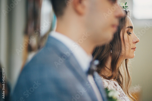 Stylish bride and groom standing during holy matrimony in church. Wedding ceremony in cathedral. Classic spiritual wedding couple with burning modern candles