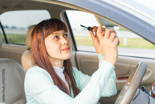 Young woman looking in rear view mirror and making up her mascara while sitting behind the wheel of her car. Female painting mascara doing applying make up while driving. Concept of danger driving. © Patcharanan