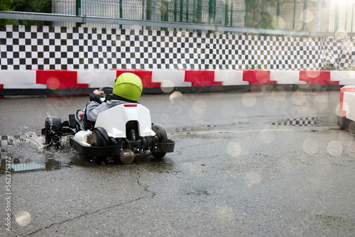 Child racer in a helmet driving an electric car drives into a sharp turn of a go-kart track. Children's karting competitions on a professional track