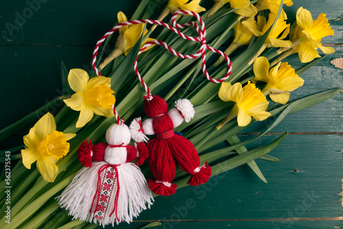 Martenitsa, Martisor on a bouquet of yellow daffodils on a green wooden table top view photo