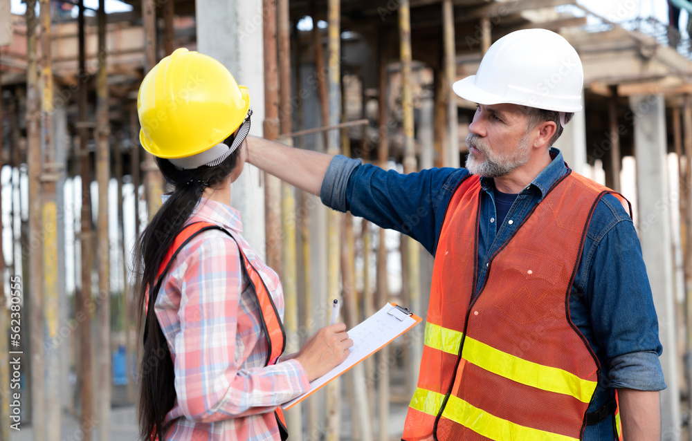Construction engineers working at real estate site with construction scaffolding background. Junior engineer taking note of improvement items to inform foreman and worker Construction engineers working at real estate site with construction scaffolding background. Junior engineer taking note of improvement items to inform foreman and worker