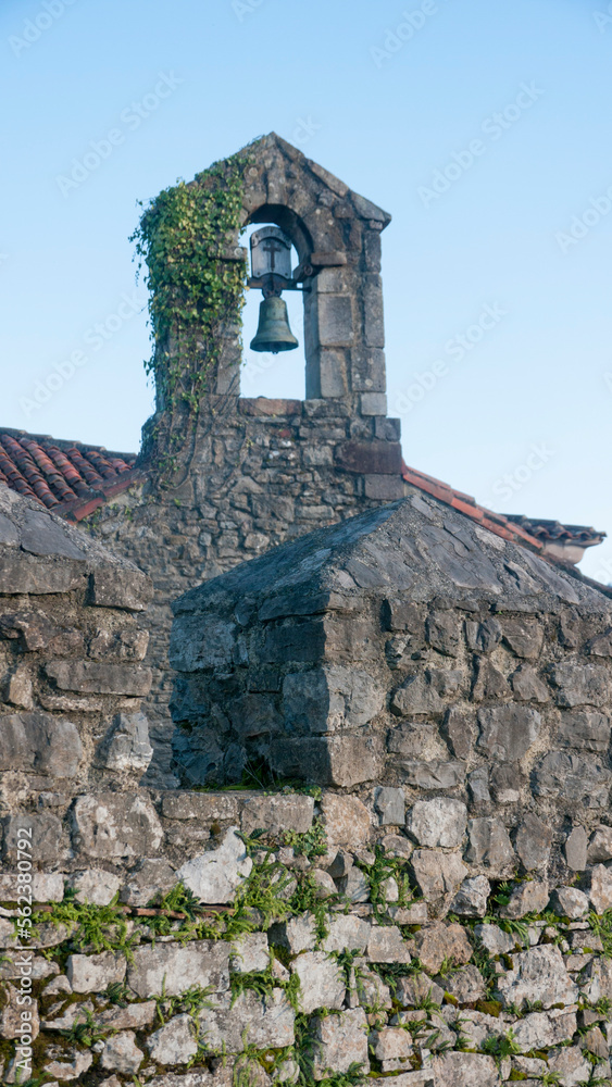 Campanario de iglesia románica de piedra tras almenas de muralla en zona rural de Asturias