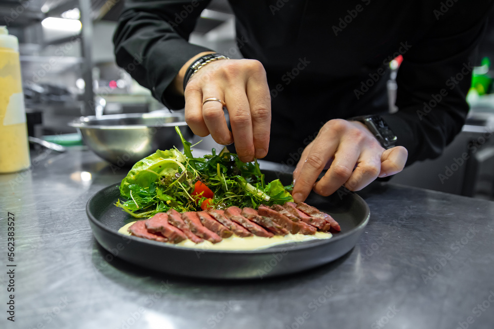 chef hand cooking Roast beef salad with vegetables on restaurant kitchen