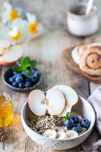 Healthy breakfast, oatmeal or granola with blueberries, apple and honey on a rustic wooden background