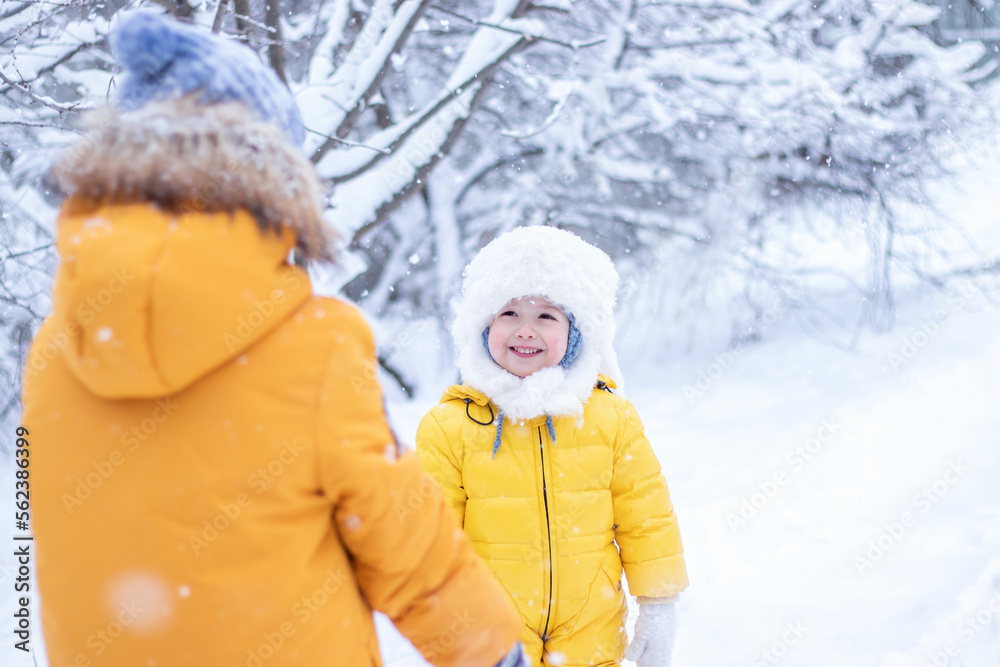 Happy children in warm yellow outwear walking together on winter snowy vacation. Two of kid friends looking each other, having fun in park Happy children in warm yellow outwear walking together on winter snowy vacation. Two of kid friends looking each other, having fun in park