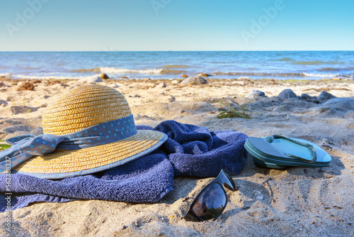 Straw hat and flip flops on a blue towel on the natural beach on the sea, tourist resort on the Baltic Sea in Germany, sunny summer vacations, copy space, selected focus