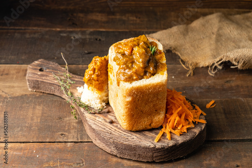 African national dish bunny chow in white bread close-up. Meat and vegetable curry served with carrot salad.