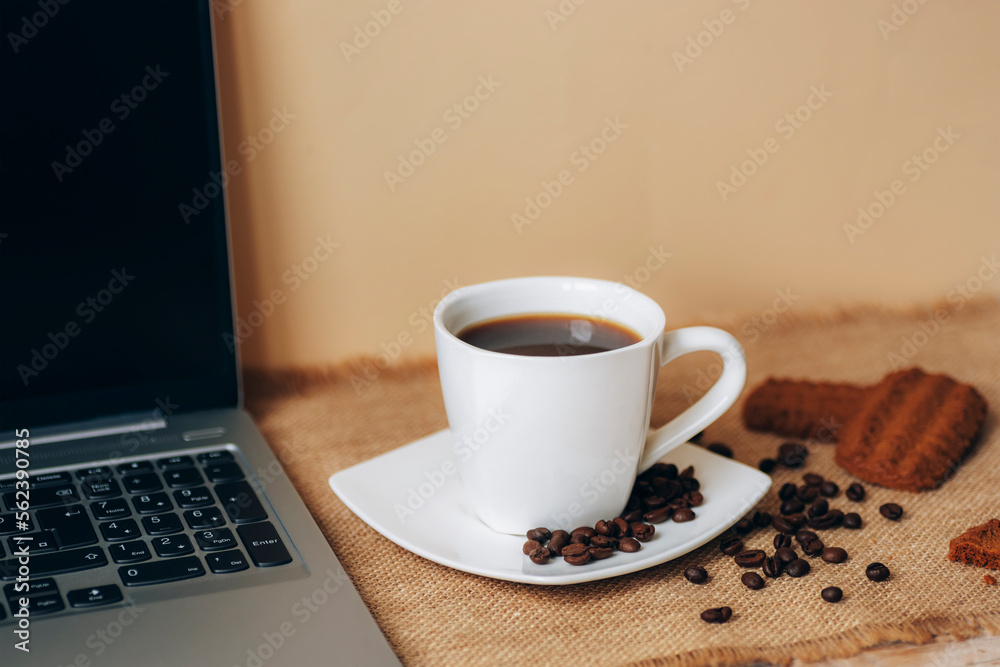 Coffee cup with beans, cookies and laptop on beige table Coffee cup with beans, cookies and laptop on beige table