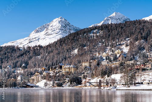 View of the town of St. Moritz during winter in the shade with snow covered mountains in background on a sunny day in Switzerland.