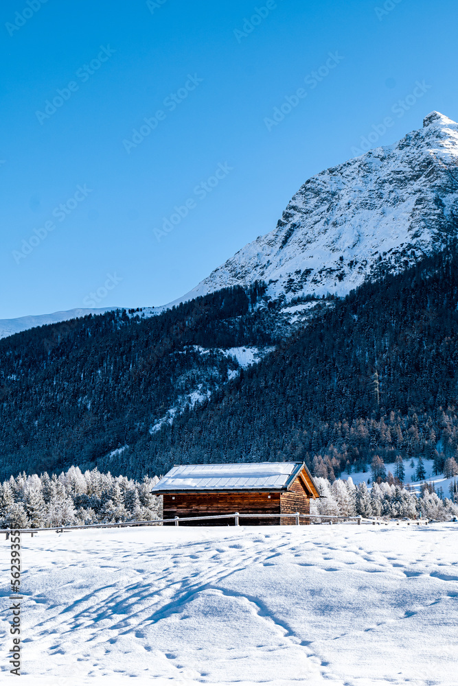 Wooden hut in between mountains covered in snow during winter on a sunny day in Switzerland.