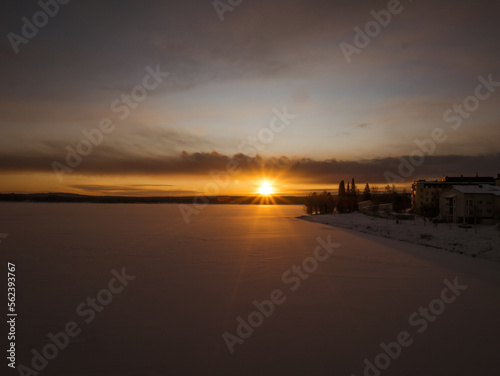 Sunset behind a snowy forest landscape and frozen river in Rovaniemi, Finland. © Patrick Pimienta