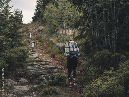 Young caucasian woman hiking with a backpack through a rocky trail in a forest.