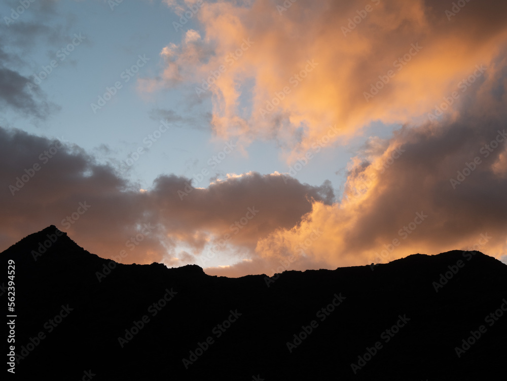 Sunset orange clouds rolling over mountain.