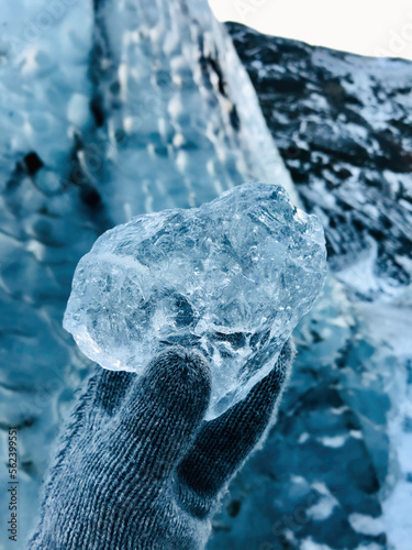 Fototapeta Naklejka Na Ścianę i Meble -  Hand with Glove Holding Icelandic Glacier Frozen Ice Chunk, Nordic Nautre Winter POV