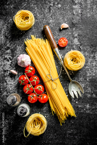 Raw spaghetti and tagliatelle with cherry tomatoes, garlic and a ladle.