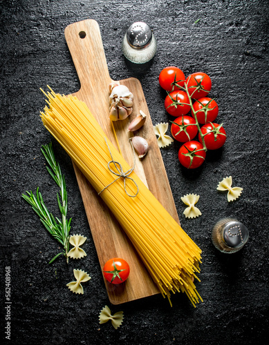 Raw spaghetti on a wooden cutting Board with garlic, tomatoes and rosemary.