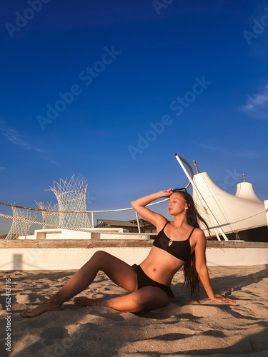 A young beautiful woman with long hair in a swimsuit dreamily looks at the beach with the sea in the background