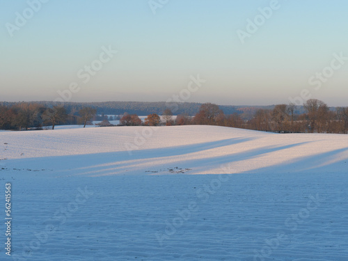 Mit Schnee bedeckte Felder im Winter mit langen Schatten von Bäumen photo