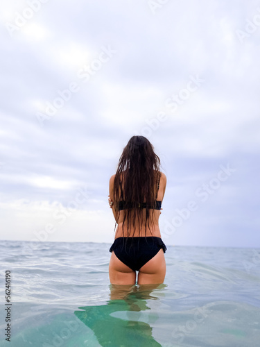  beautiful woman with long hair in a bikini dreamily looks at the beach and rests with the sea in the background