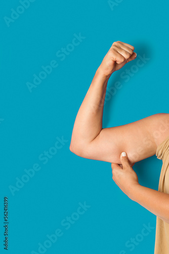 Mujer gorda sosteniendo su brazo con exceso de grasa. sobre un fondo turquesa liso y aislado. Vista de frente y de cerca. Copy space. Formato vertical photo