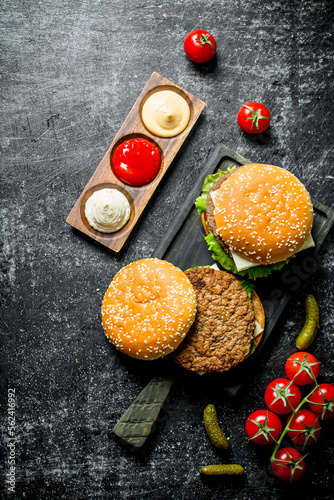 Burgers with French fries, gherkins,tomatoes and different sauces.