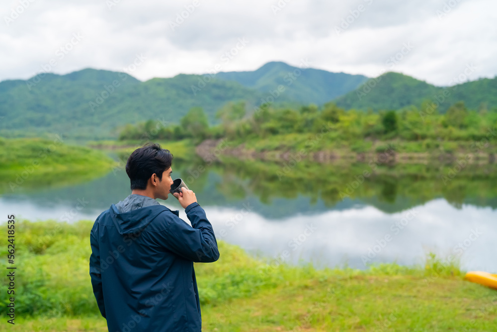 Asian man relax and enjoy outdoor lifestyle hiking and camping in forest mountain while travel on summer holiday vacation trip. Handsome guy brewing and drinking hot coffee by the lake in morning. Asian man relax and enjoy outdoor lifestyle hiking and camping in forest mountain while travel on summer holiday vacation trip. Handsome guy brewing and drinking hot coffee by the lake in morning.